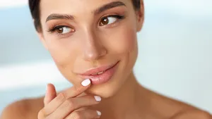 Vrouw raakt haar mond aan terwijl ze hyaluronzuur op haar lippen gesmeerd heeft.