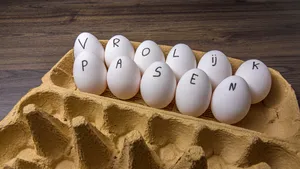 Een geopende eierdoos met witte eieren, waarop met de hand de tekst 'Vrolijk Pasen' is geschreven als versiering voor het paasontbijt.