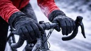 Close-up van een fietser met dunne winterhandschoenen die verkrampte handen om het stuur klemt, met rijp op de fiets en een ademwolk in de ijskoude lucht.