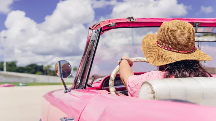 Unrecognizable woman driving retro cabriolet on city road