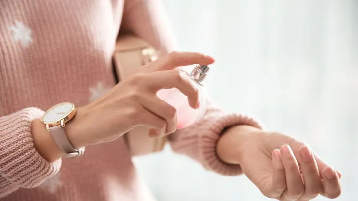 Vrouw spuit parfum op huid.