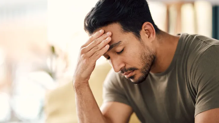 Tired, headache and stress of man in living room with mental health, fatigue and sad problem. Face, depression and frustrated male person with anxiety, brain fog or crisis of failure, mistake or debt