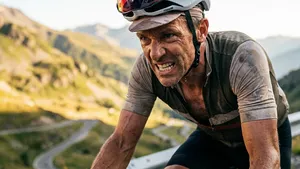 Een ervaren wielrenner beklimt een steile weg op zijn racefiets, met een vastberaden uitdrukking van inspanning op zijn gezicht.