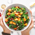 Vegetable salad bowl in woman hands. Fresh kale and baked pumpkin salad. Healthy eating concept