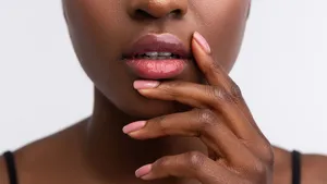 African-American woman touching lips with shiny lip gloss