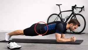 Wielrenner in wielerbroek en wielershirt plankt op sokken, met een subtiel ingezakte houding ter hoogte van de onderrug.