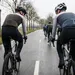 Een groep wielrenners in winterkleding rijdt in peloton op een natte polderweg in Nederland.
