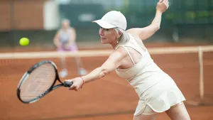 Een gepassioneerde vrouw op leeftijd, van achteren gezien, die tijdens een vriendschappelijk potje tennis in de zomer op het punt staat om de bal met een forehand terug te slaan naar haar tegenstander