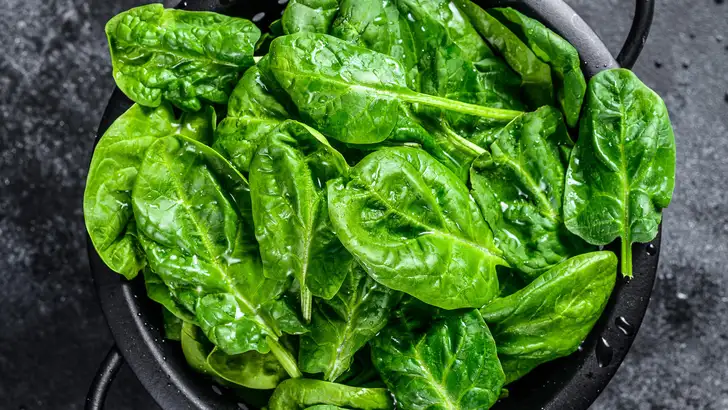 Young raw spinach in a colander. Black background. Top view