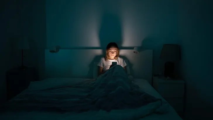 Sleepy woman lying in bed using smartphone late at night, can not sleep. Insomnia, addiction concept