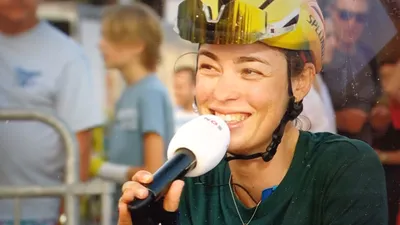 Mischa Bredewold lacht tijdens een interview voor de NOS, waarbij ze haar fietshelm nog op heeft om platgeslagen helmhaar te verbergen.
