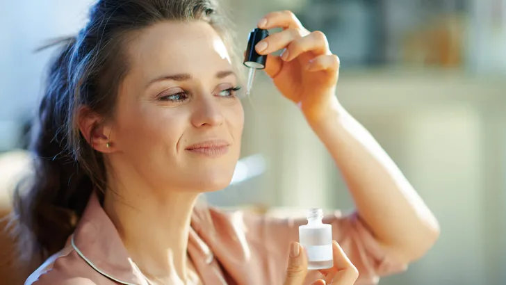 woman in modern house in sunny winter day using cosmetic elixir