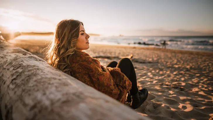 Young woman sitting by a beach at sunset in winter