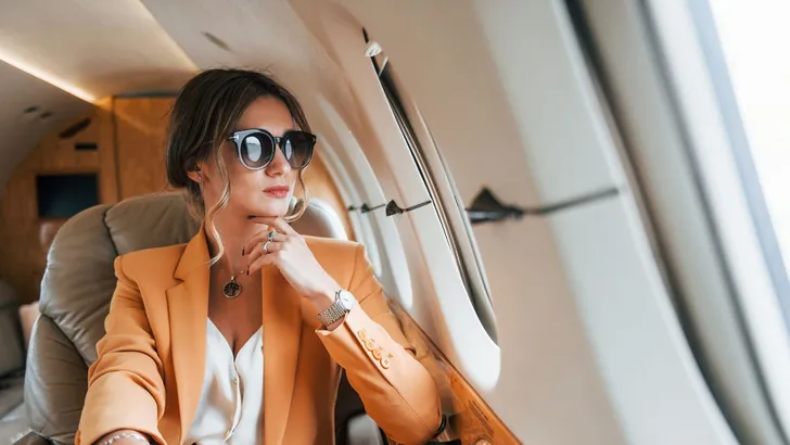 Een vrouw die vanuit het vliegtuigraampje naar buiten kijkt - Dít gebeurt er met je huid tijdens een vlucht – en zo pak je het aan
