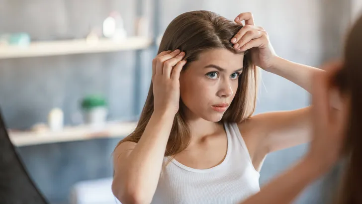 Pretty girl with hair loss problem looking in mirror at home