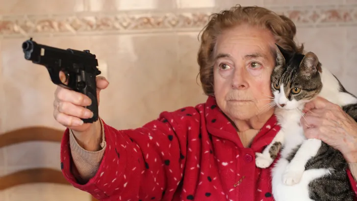 Boze oudere vrouw beschermt haar kat met een pistool.