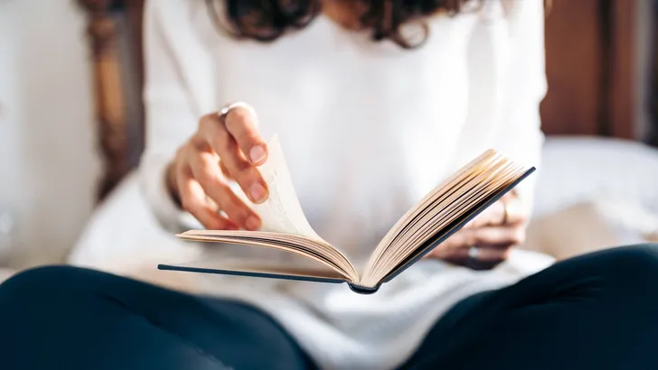 Unrecognizable young woman turning the pages of a book while reading in bed