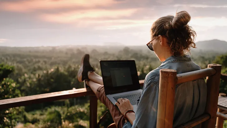 Young business woman working at the computer in cafe on the rock. Young girl downshifter working at a laptop at sunset or sunrise on the top of the mountain to the sea, working day.