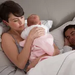 Mother Cuddling Newborn Baby In Bed At Home