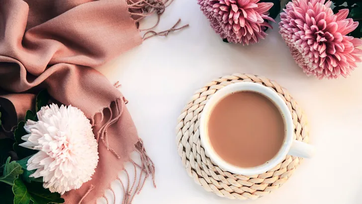 A cup of coffee, pink scarf and chrysanthemum flowers on white table. Cozy home, breakfast concept. Top view, flat lay