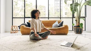 Young multiracial latina woman meditating at home with online video meditation lesson using laptop.