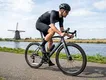 en wielrenner op snelheid op een Specialized brand moderne carbon racefiets met schijfremmen en geïntegreerde cockpit, rijdend op een Nederlands fietspad langs een kanaal met een molen in de polder.