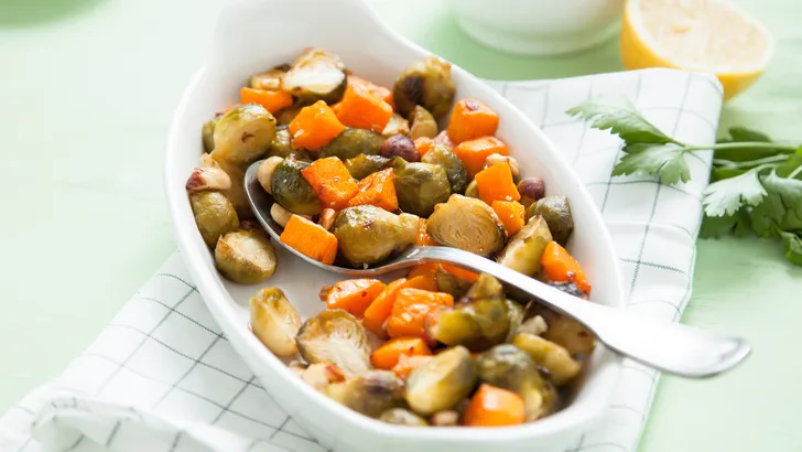 Ovenschaal met spruitjes en pompoen op een theedoek.