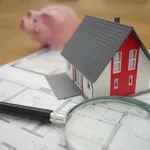 Beleggen in vastgoed. – Foto van miniatuur-huisje op plattegrond bij spaarvarken.