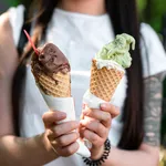 Female hands are holding two melting gelato. chocolate and pistachio flavor in the cones.