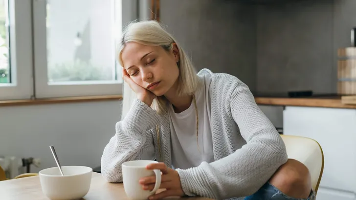 sleepy caucasian woman drinking morning coffee in her kitchen