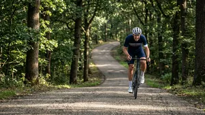 Mannelijke wielrenner met helm fietst zwoegend omhoog op een steile, rustige bosweg in Nederland.