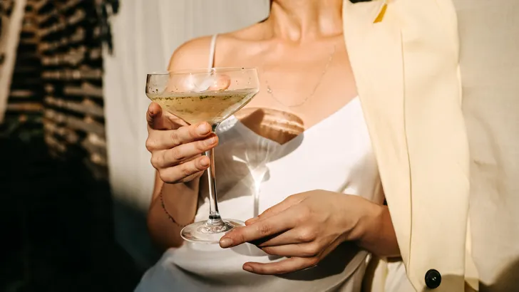 Beau Monde's tips voor het weekend. – Foto van vrouw in witte blazer met cocktail in hand.