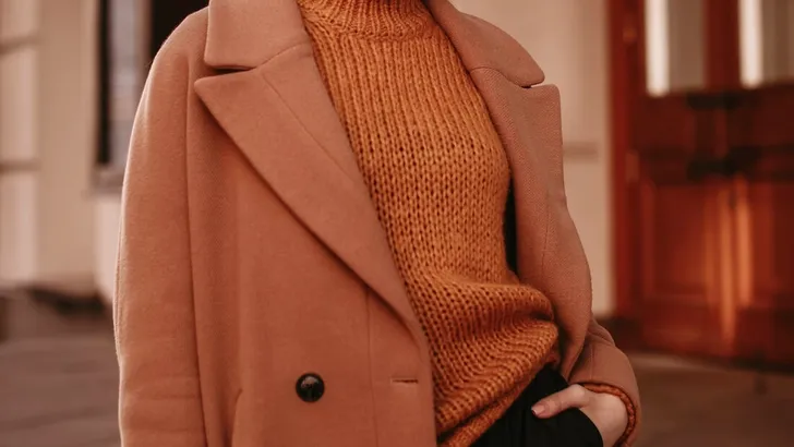 Young woman  with cropped head in the orange knitted cozy sweater and brown coat standing on the street. Outdoor portrait in daylight. Autumn casual fashion style