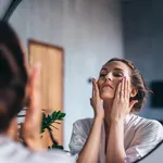 Woman applies foam to her face, cleansing her skin.