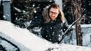 Man die ondergesneeuwde auto schoonmaakt.