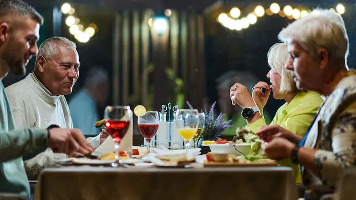 A group of family friends, comprising a young grandson and older individuals, share a delightful dinner in a modern restaurant, exemplifying the concept of healthy aging through intergenerational bonding and a joyous dining experience