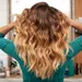 Dit kapsel zorgt voor extra volume bij fijn haar. – Foto van vrouw met lang golvend haar voor spiegel.