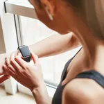 What time is it? Cropped photo of young woman in sportswear checking the time on her sport bracelet while standing in front of window at gym