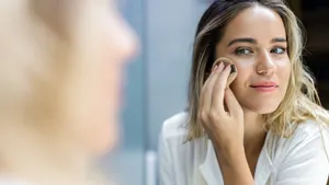 Reflection in a mirror of a woman applying face powder in bathroom.