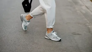 Detailopname van de voeten van een vrouw in witte sneakers, wandelend over het asfalt van een straat in de stad.