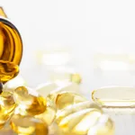 Many nutritional health supplement fish oil capsules spilling out of their bottle onto a white wood table background, shallow depth of focus.