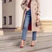 Streetstyle-foto van stijlvolle vrouw in spijkerbroek, pumps en beige trenchcoat.