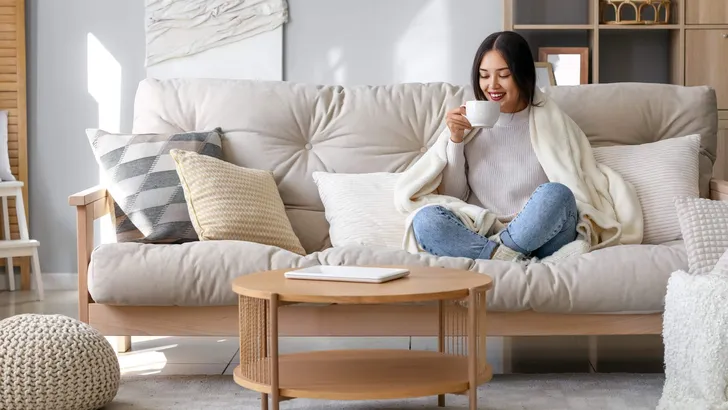 Young Asian woman with warm plaid drinking tea at home