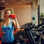 Beautiful young woman resting and drinking water in the gym