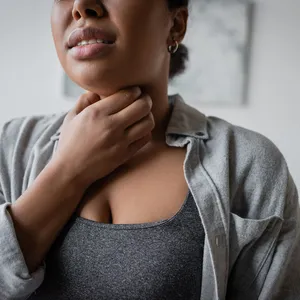 Bijgesneden afbeelding van een jonge vrouw van gemengde afkomst die thuis haar keel aanraakt.