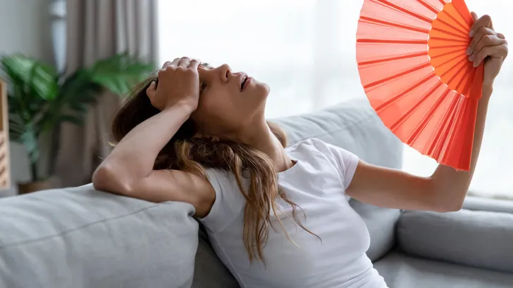 Exhausted girl using paper waver, suffering from hot summer weather.