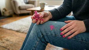 Een close-up van een persoon in een blauwe spijkerbroek met een kleine, verse roze nagellakvlek.
