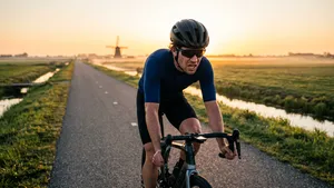 Een uitgeputte wielrenner met helm rijdt vermoeid op zijn racefiets tijdens een nuchtere ochtendtraining zonder ontbijt.