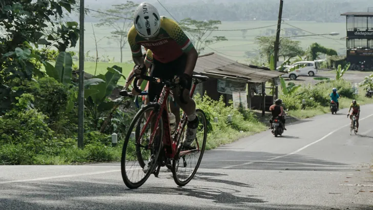 Dynamische actiefoto van een wielrenner die krachtig en in balans staand op de pedalen een berg beklimt, waarbij de fiets kantelt onder de rijder.
