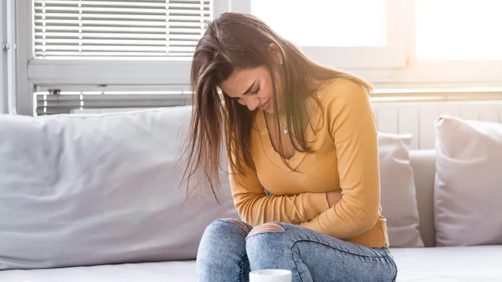 Woman lying on sofa looking sick in the living room. Beautiful young woman lying on bed and holding hands on her stomach. Woman having painful stomachache on bed, Menstrual period